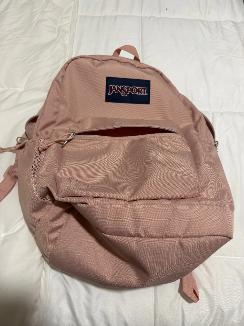 JanSport Cross Town backpack in a light pink color with a blue logo patch